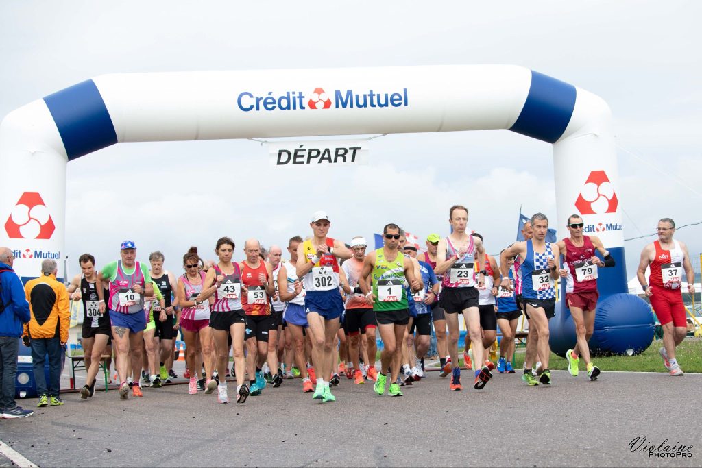 Départ d’un 10km Marche avec un groupe de coureurs sous une arche Crédit Mutuel marquée 'DÉPART'.